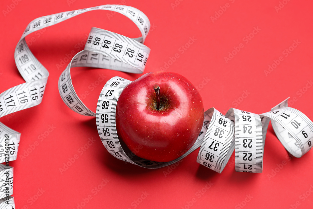 Apple and measuring tape on red background, closeup. Diet concept