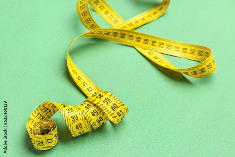 New yellow measuring tape on green background, closeup