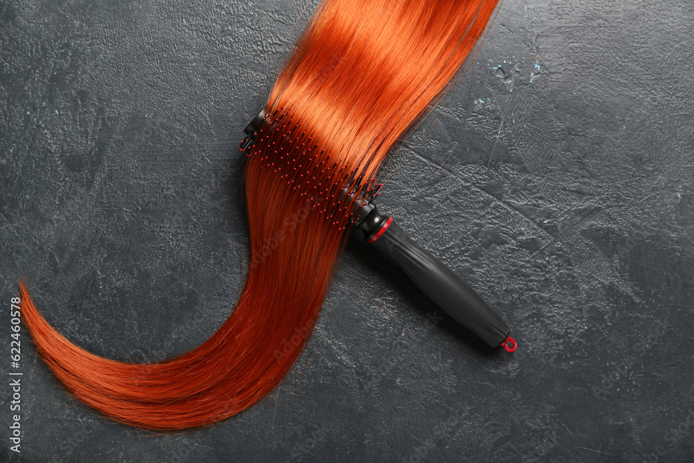 Ginger hair strand and brush on dark background, closeup