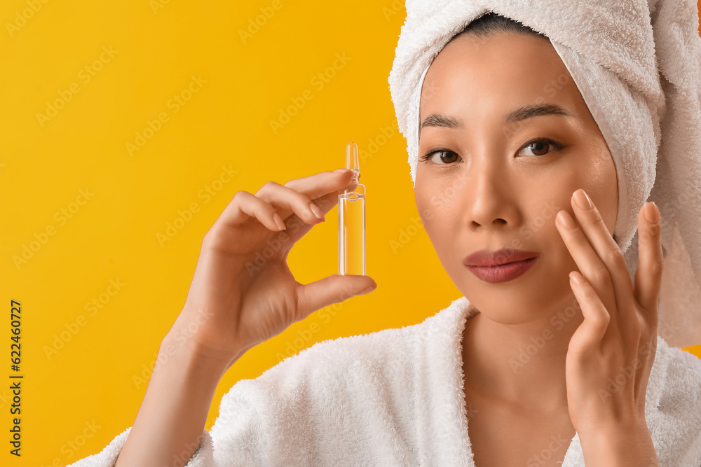 Beautiful Asian woman with ampule on yellow background. Skin care concept