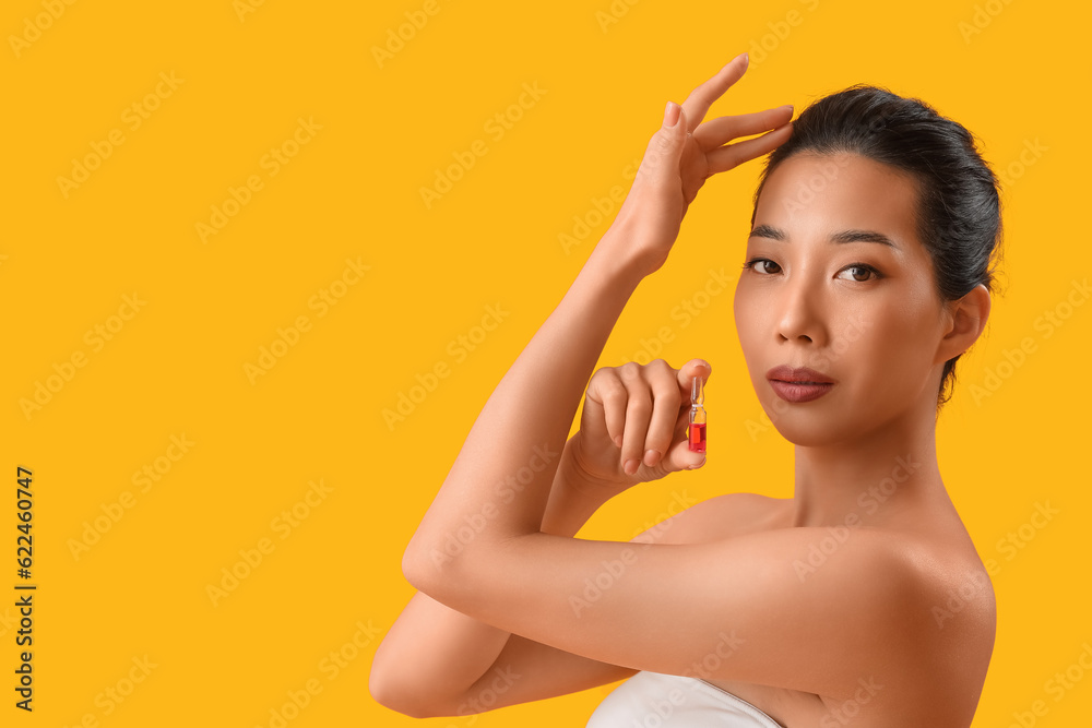 Beautiful Asian woman with ampule on yellow background. Skin care concept