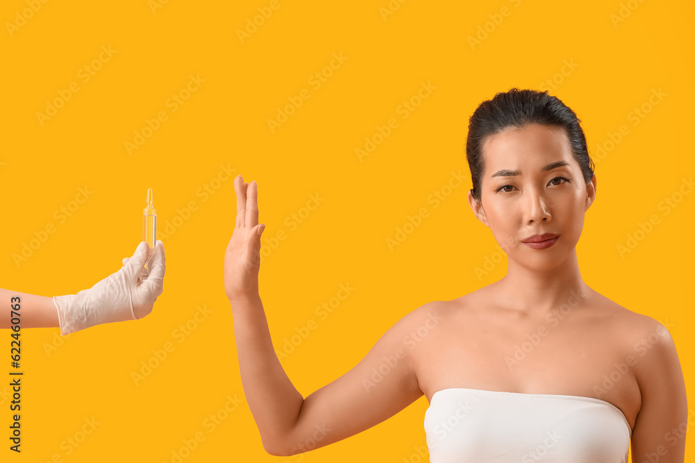 Beautiful Asian woman rejecting ampule on yellow background. Skin care concept