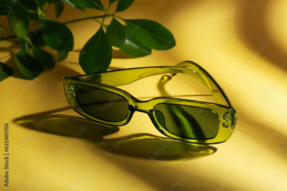 Stylish eyeglasses and branch on yellow background, closeup