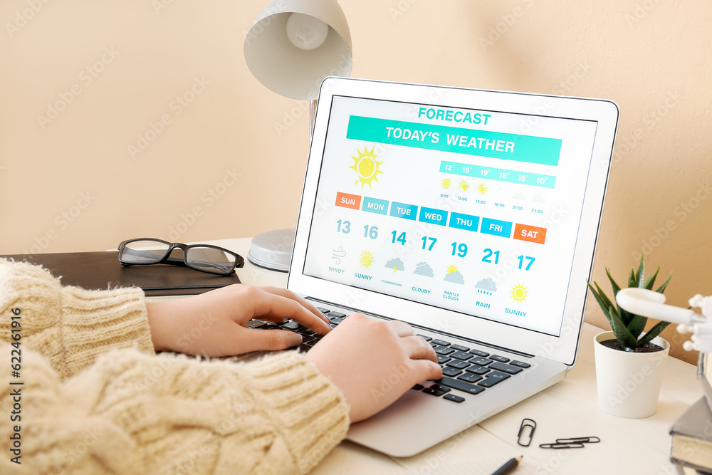 Woman with laptop checking weather forecast at table, closeup