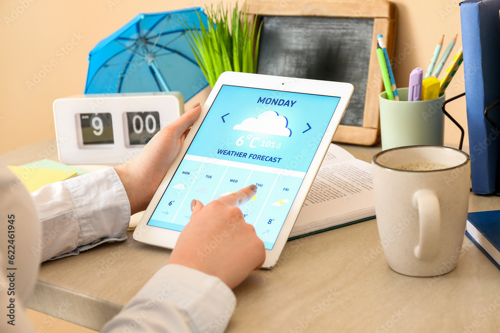 Woman with tablet computer checking weather forecast at table, closeup