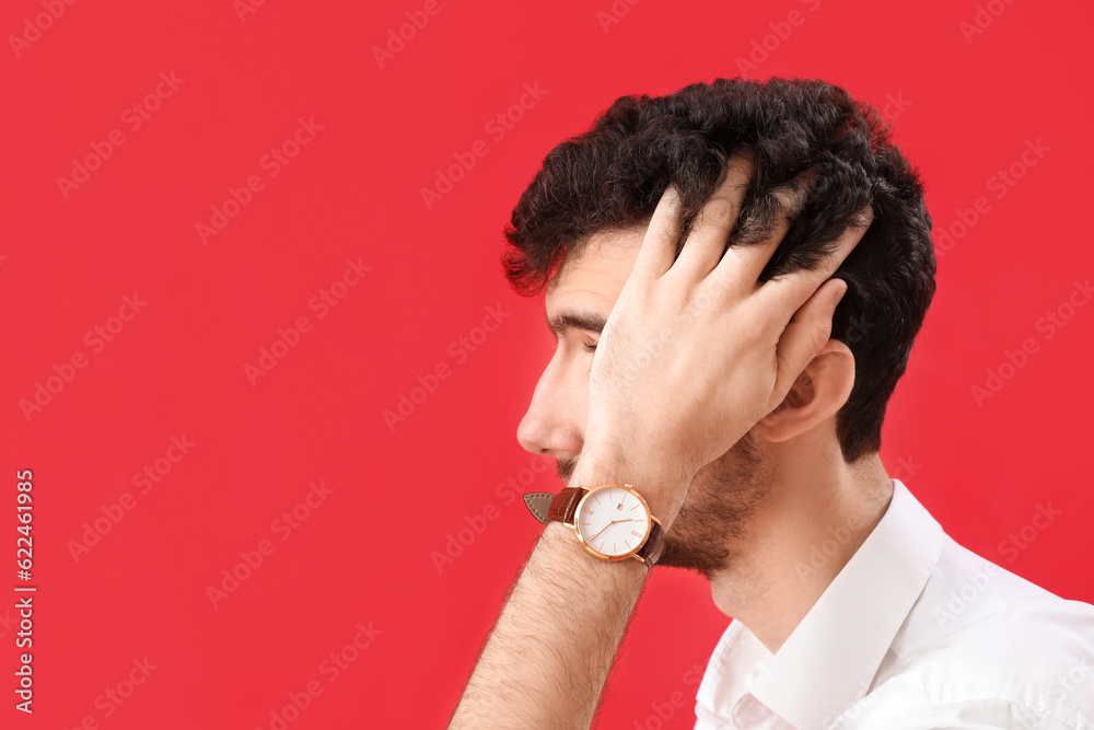 Young brunette man with stylish hairdo on red background, closeup