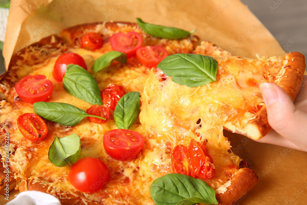 Female hand taking slice of tasty pizza margarita on parchment, closeup