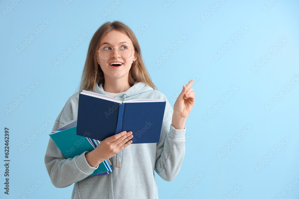 Happy female student with different books pointing at something on blue background