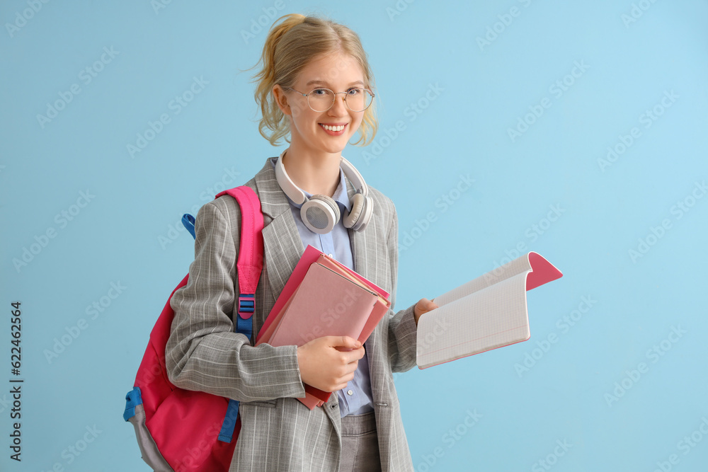 Happy female student with backpack, books and headphones on blue background