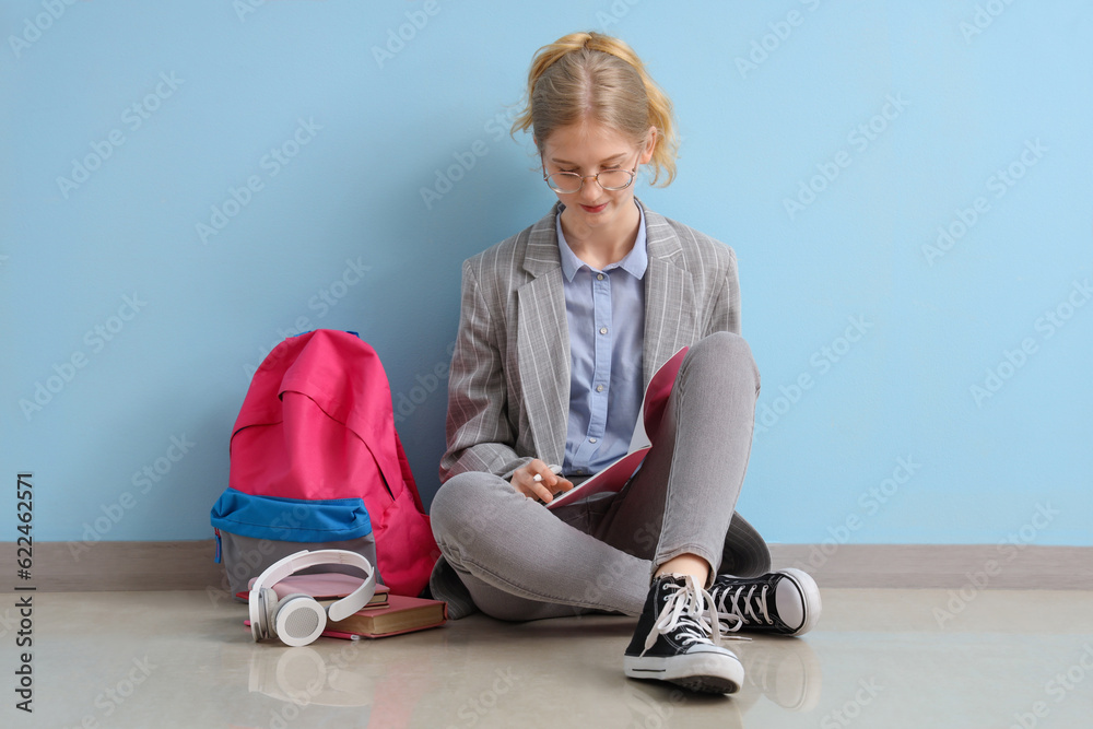 Female student with backpack and headphones sitting near blue wall