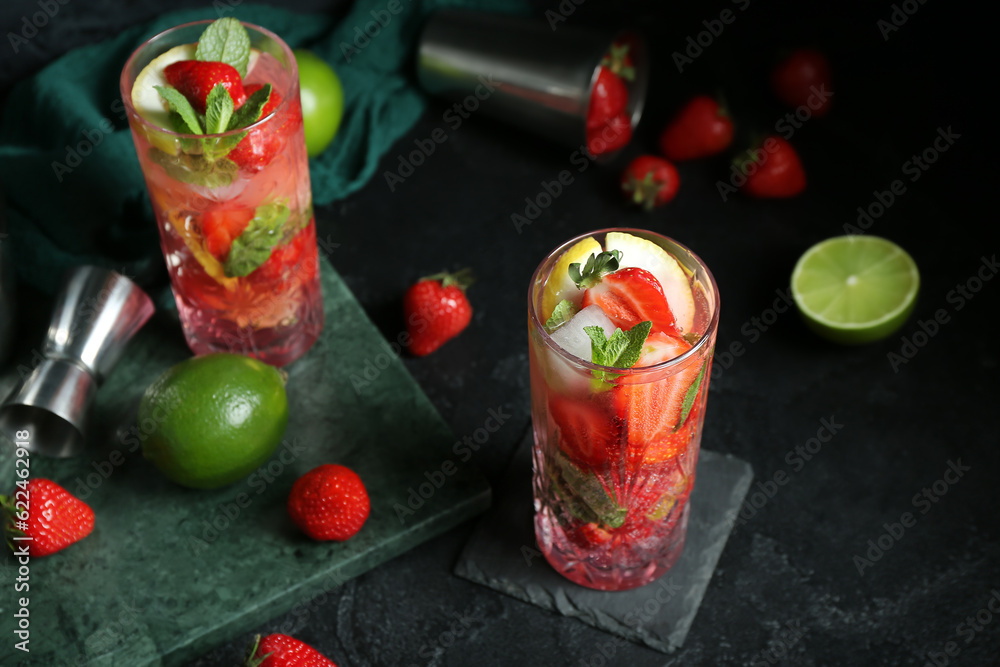 Stands with glasses of fresh strawberry mojito, jigger and shaker on black background