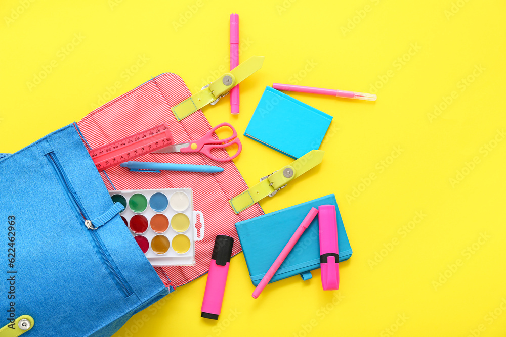 Blue school backpack with notebooks, markers and watercolors on yellow background