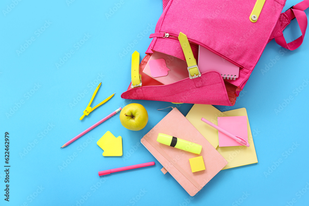 Pink school backpack with notebooks, stickers and apple on blue background