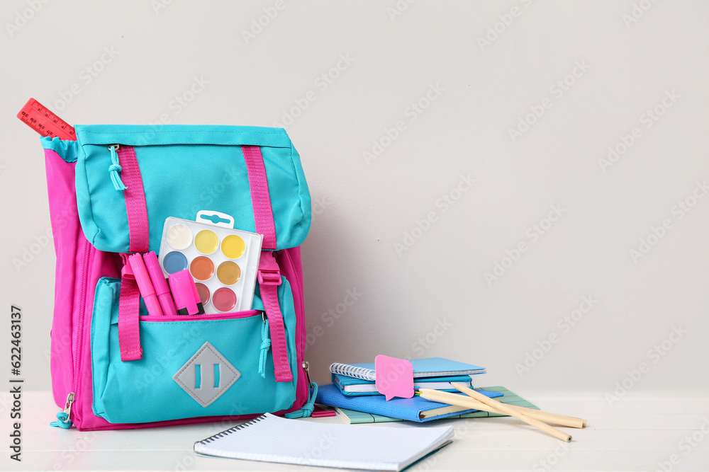 Color school backpack with notebooks, watercolors and markers on white wooden table near wall