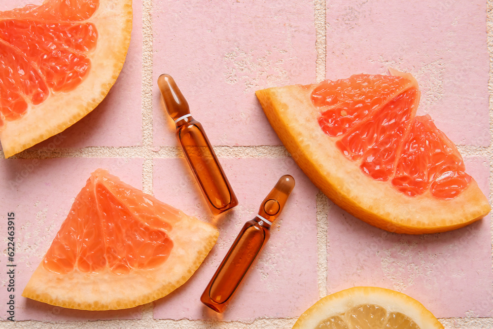 Ampoules with vitamin C and different citrus fruit slices on pink tile background