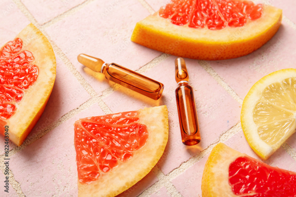 Ampoules with vitamin C and different citrus fruit slices on pink tile background