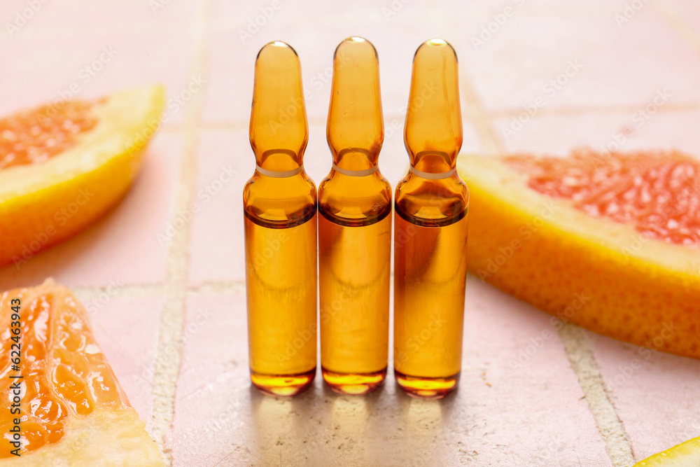 Ampoules with vitamin C and grapefruit slices on pink tile background