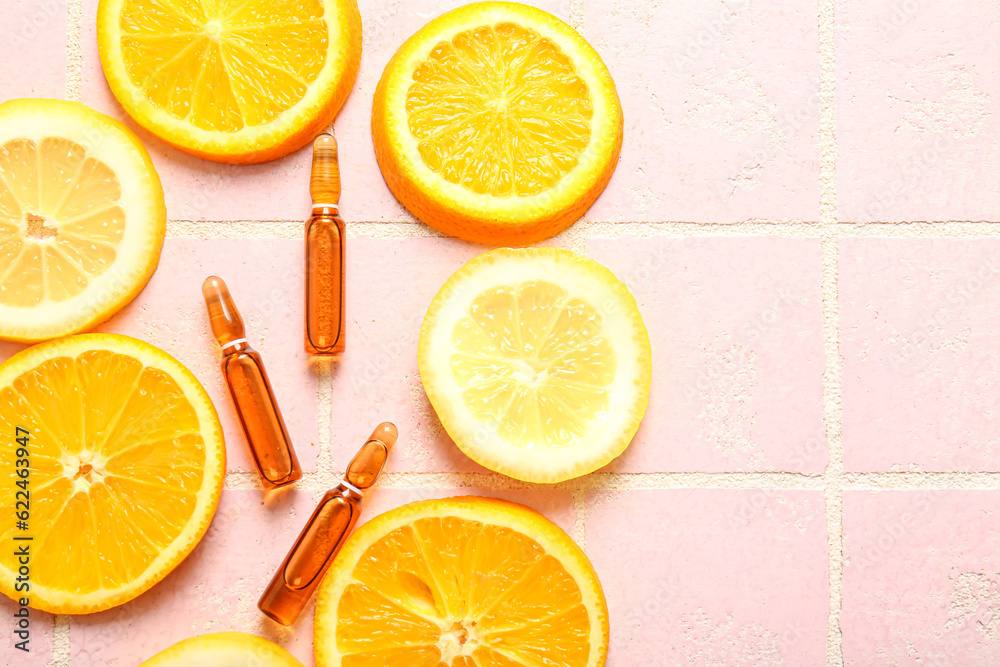 Ampoules with vitamin C and different citrus fruit slices on pink tile background