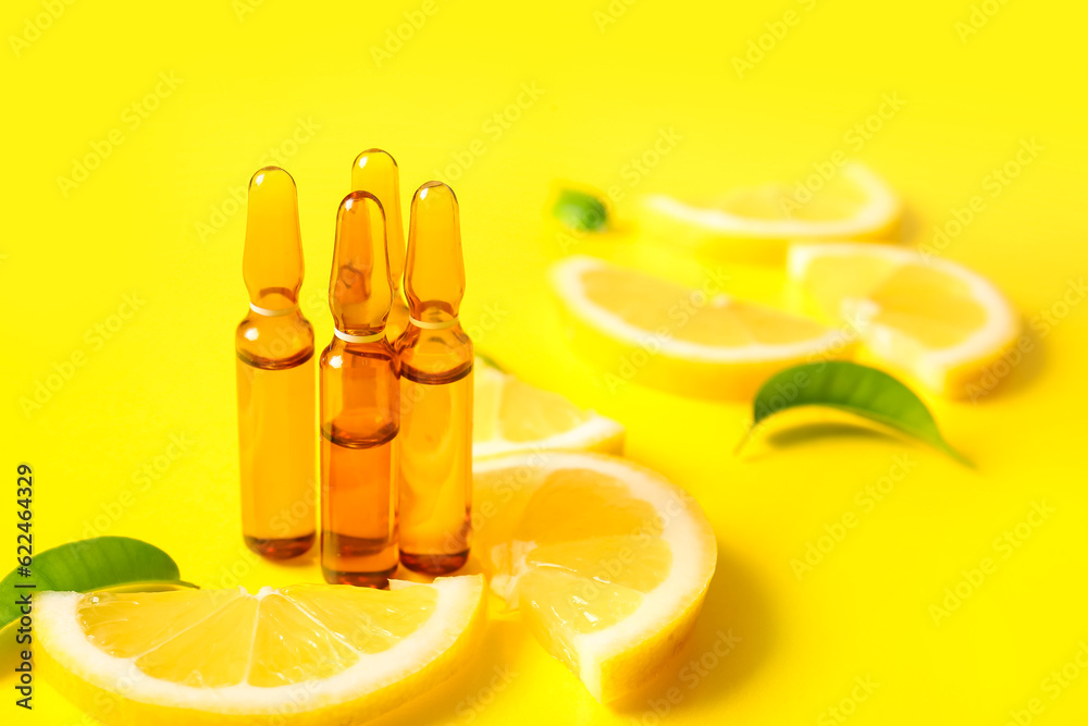 Ampoules with vitamin C and lemon slices on yellow background, closeup