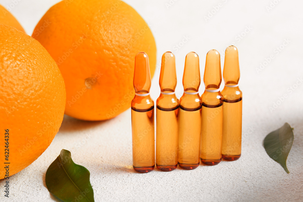 Ampoules with vitamin C and oranges on light background, closeup