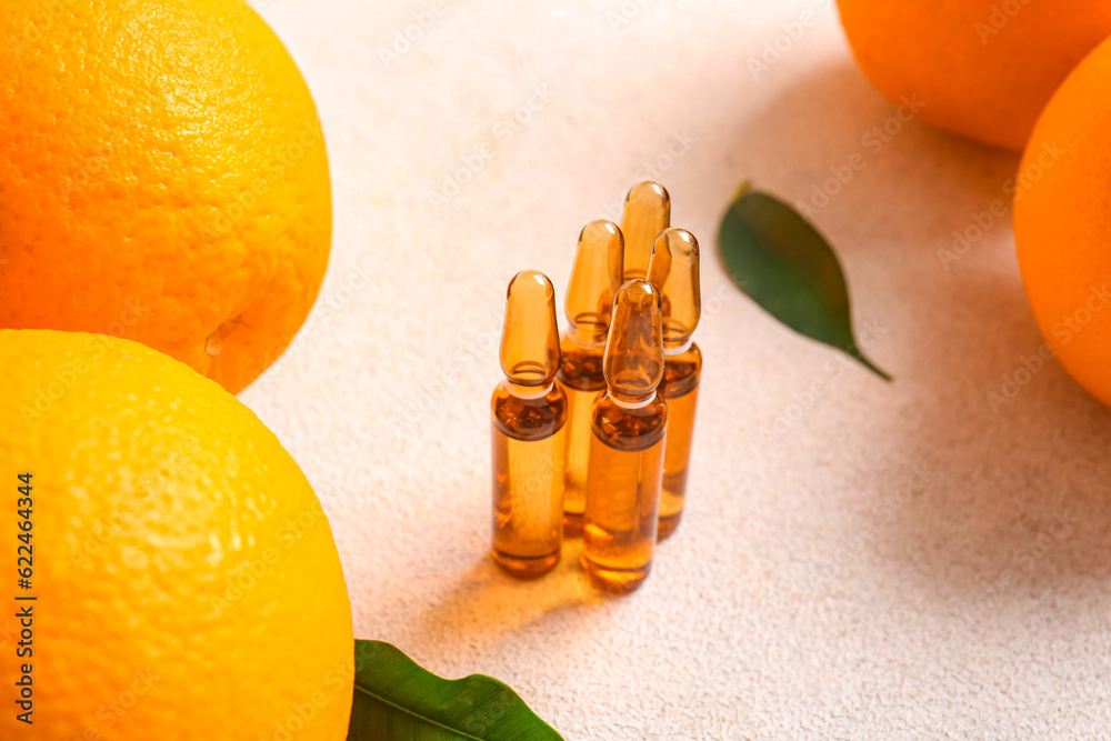 Ampoules with vitamin C and oranges on light background, closeup