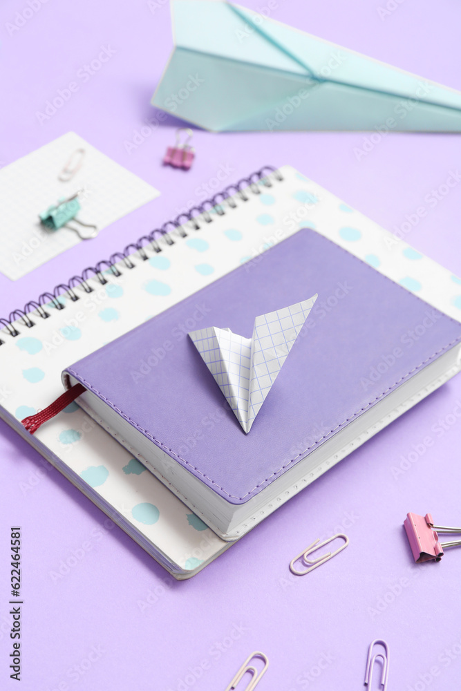 Notebooks, paper planes and school stationery on purple background, closeup