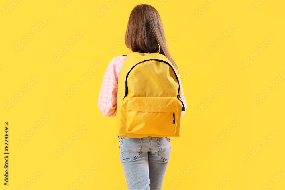 Little girl with schoolbag on yellow background, back view