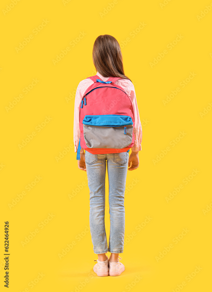 Little girl with schoolbag on yellow background, back view