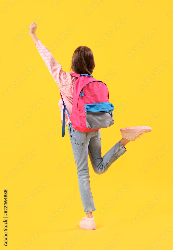 Little jumping girl with schoolbag on yellow background, back view