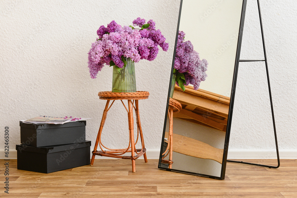 Vase with beautiful lilac flowers on table, mirror and boxes in interior of light living room