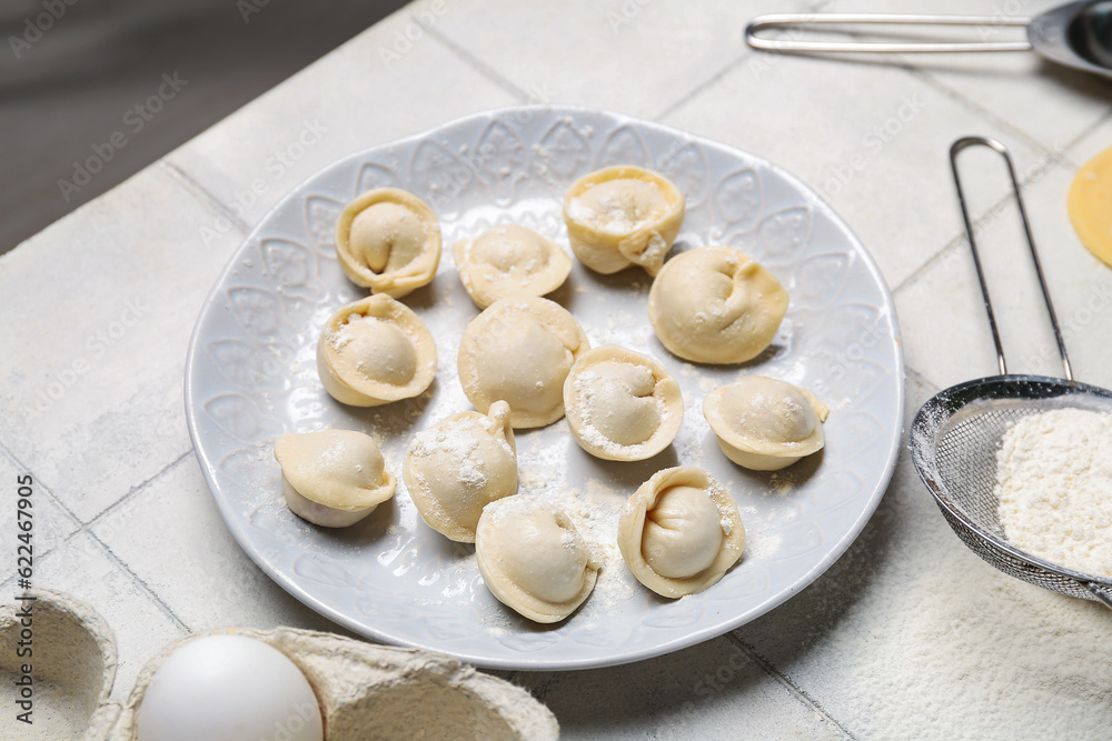 Plate with uncooked dumplings on white tile background