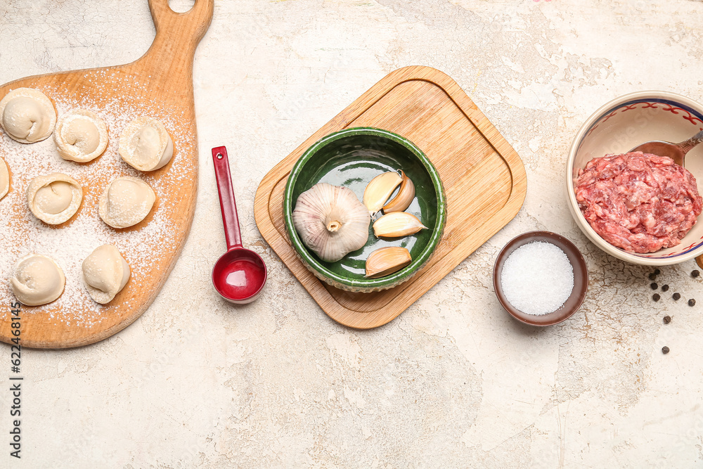 Wooden board with uncooked dumplings and ingredients on light background