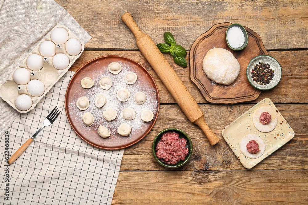 Plate with uncooked dumplings and ingredients on wooden background