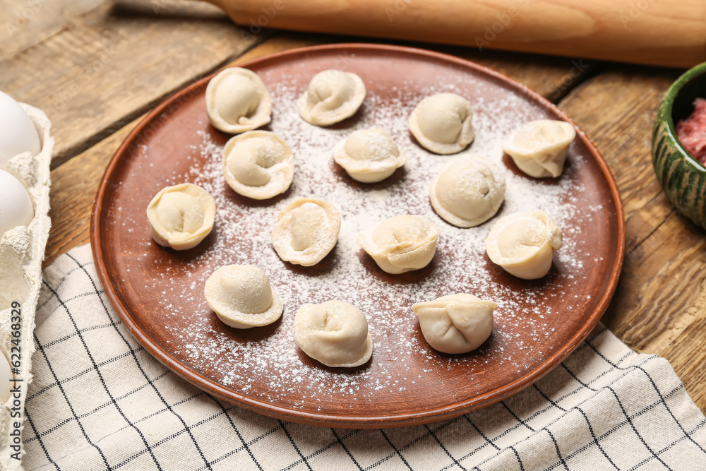 Plate with uncooked dumplings on wooden background