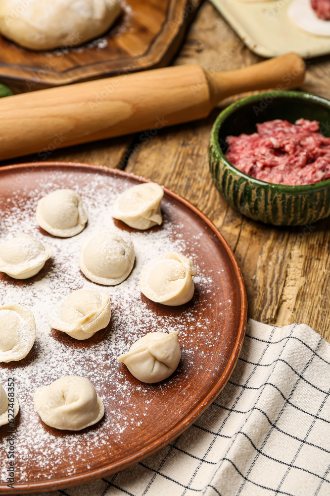 Plate with uncooked dumplings on wooden background