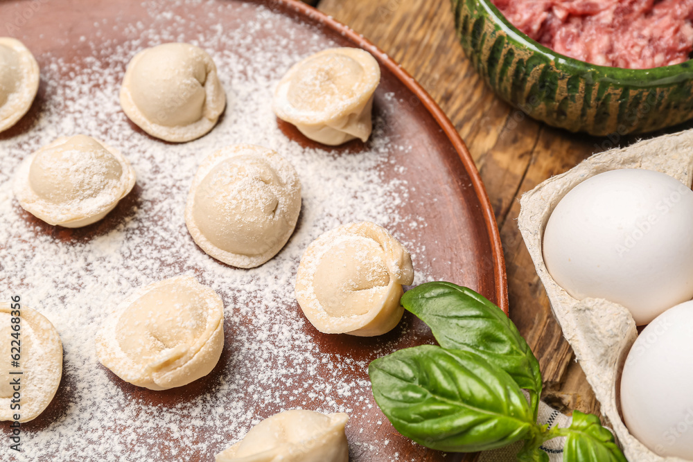 Plate with uncooked dumplings on wooden background