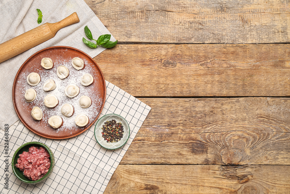 Plate with uncooked dumplings and ingredients on wooden background