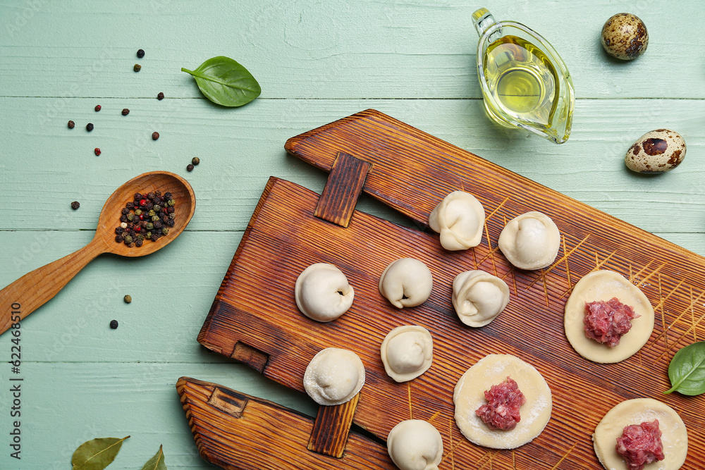 Board with uncooked dumplings on green wooden background