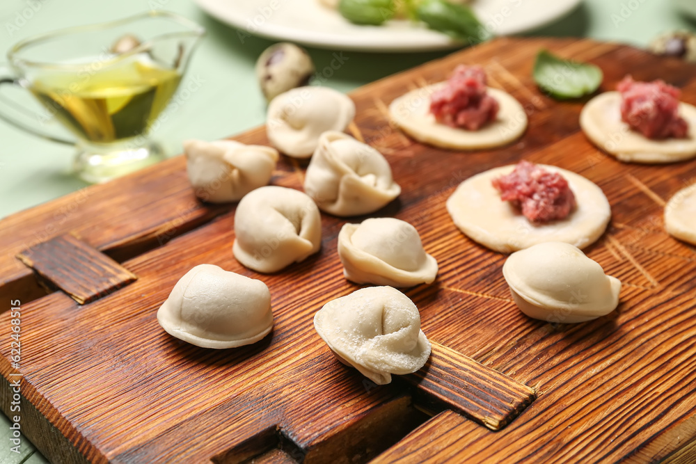 Wooden board with uncooked dumplings on table