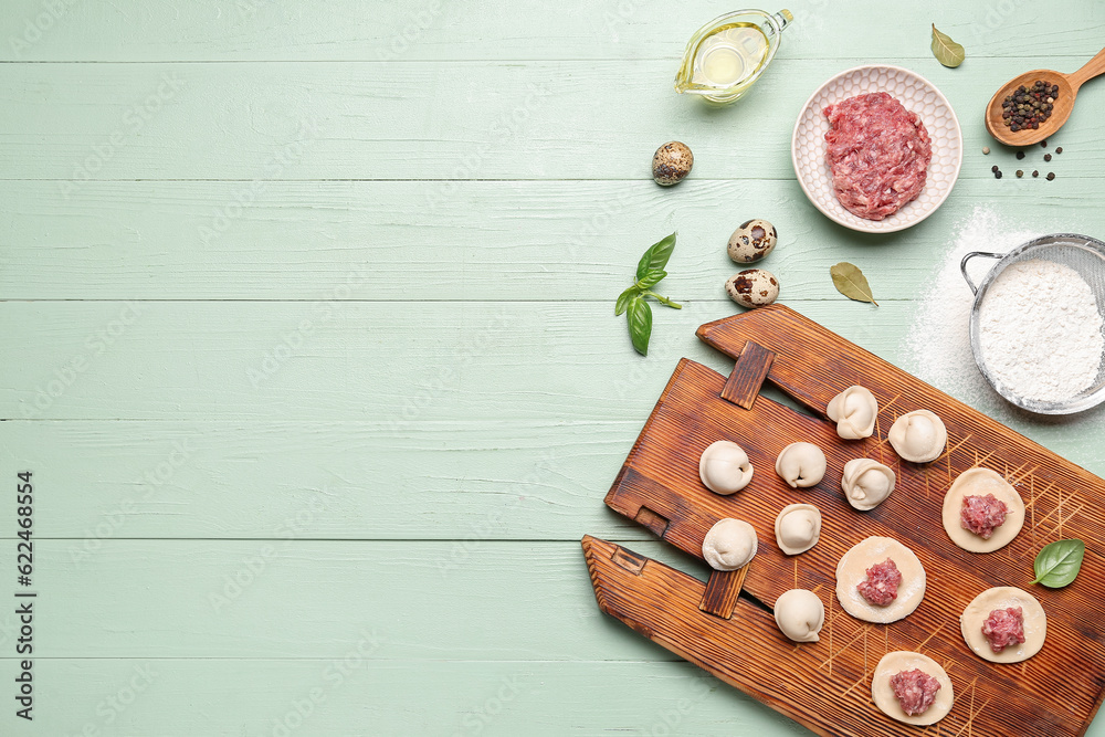 Board with uncooked dumplings and ingredients on green wooden background