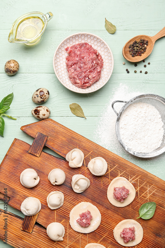 Board with uncooked dumplings and ingredients on green wooden background