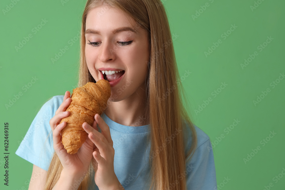 Young woman eating tasty croissant on green background, closeup