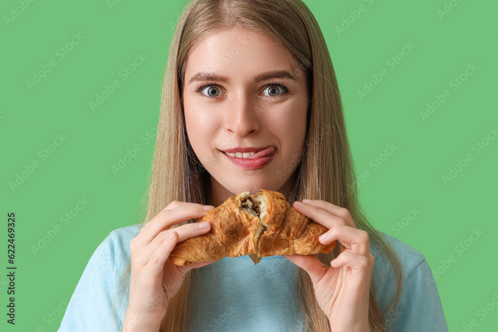 Young woman with tasty croissant on green background, closeup