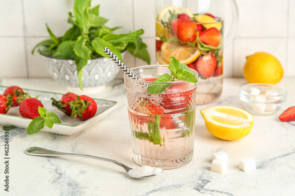 Glass and jug of fresh lemonade with strawberry on white table