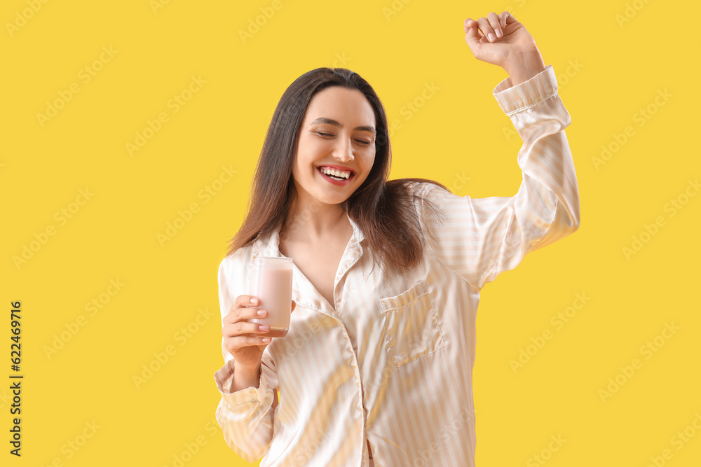 Young woman in pajamas with tasty yoghurt on yellow background