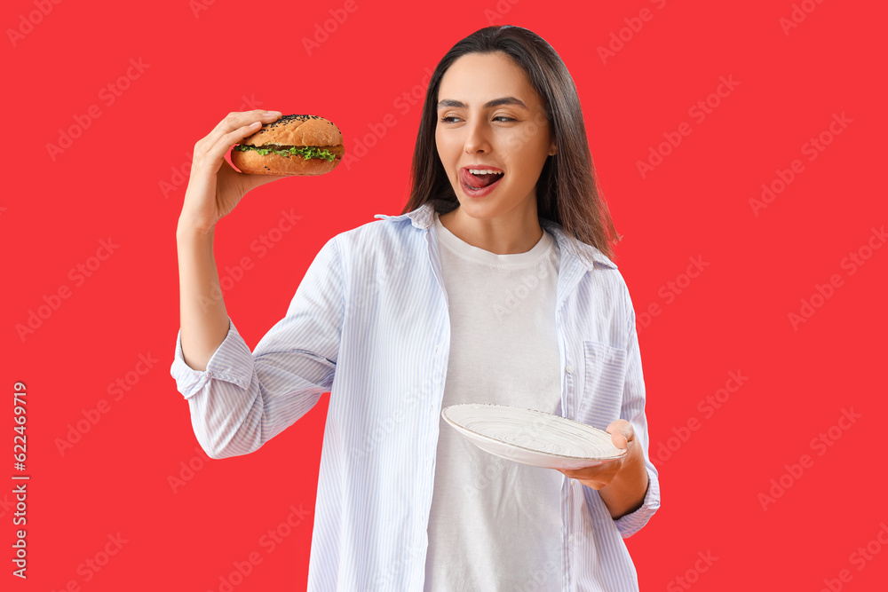 Young woman with tasty burger on red background