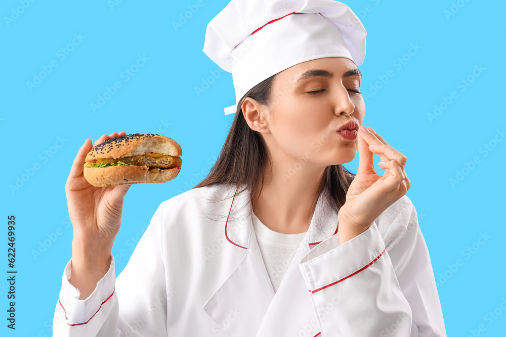 Female chef with tasty burger on blue background, closeup