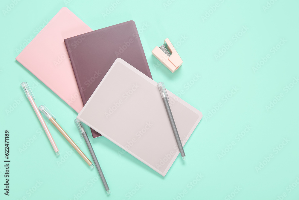 Different colorful notebooks with pens and stapler on turquoise background