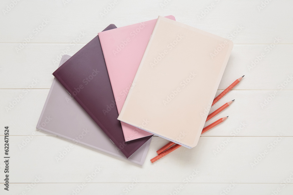 Different colorful notebooks with pencils on white wooden background