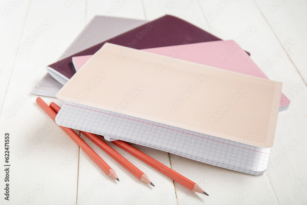 Different colorful notebooks with pencils on white wooden background